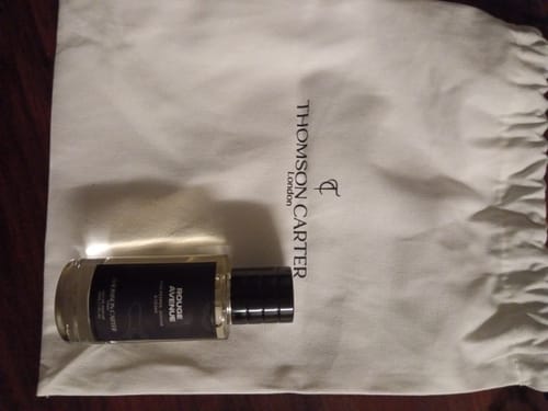 A reviewer's bottle of Rouge Avenue Eau de Parfum resting on a white cloth pouch.
