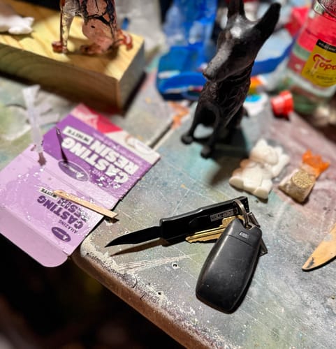 Customer's VT Mini Black Stun OTF Knife open on a keychain, resting on a workbench with resin casting supplies.