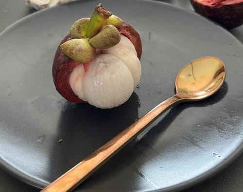 Kundenfoto einer geöffneten Mangostan auf einem dunklen Teller, die das weiße, segmentierte Fruchtfleisch freilegt.