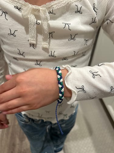 A reviewer wears the woven DAVID Bracelet on their wrist, showing its blue, green, and white pattern.