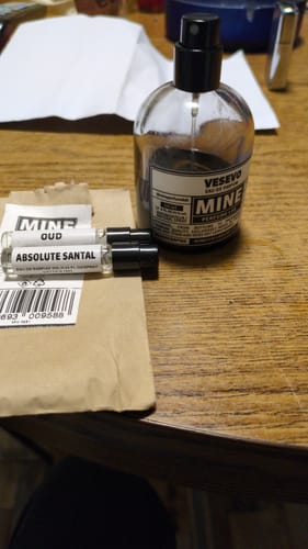 Un cliente mostra il flacone di profumo VESEVO su un tavolo di legno insieme a due campioni.