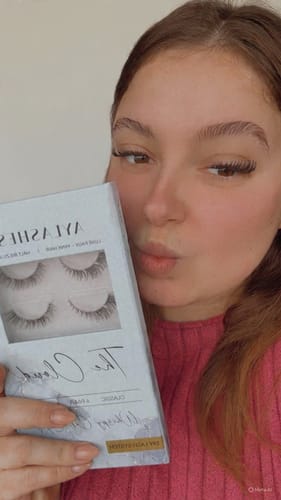Eine Kundin zeigt das Ergebnis des ALL-IN-ONE Wimpern Kits, während sie die Produktbox in der Hand hält.