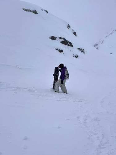 Reviewer wearing baggy beige Snow Pants and holding a snowboard on a snowy slope.