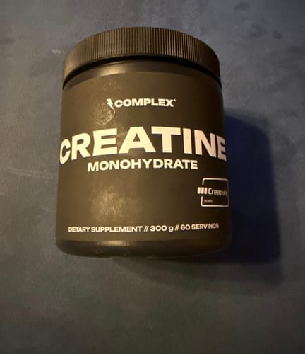 Customer's black tub of Complex Creatine Monohydrate supplement sitting on a dark surface.