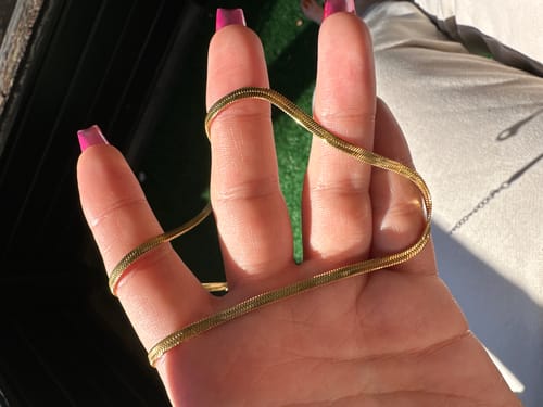 Customer's hand holding the shiny Sarya Snake Chain Gold Necklace to show its texture.