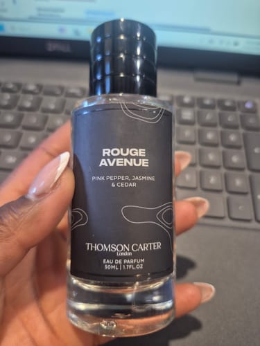 Customer's hand holding the clear bottle of Rouge Avenue Eau de Parfum with its black label.