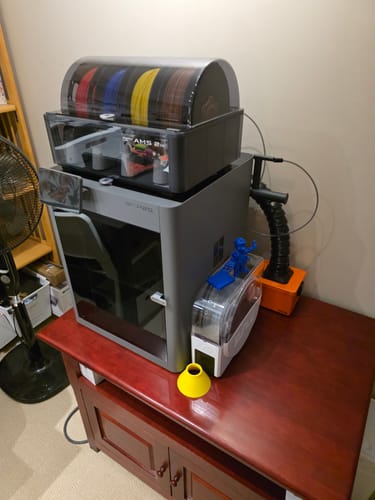 Customer's Bambu Lab P2S Combo printer set up on a wooden table, with the AMS unit loaded with colorful filament spools on top.