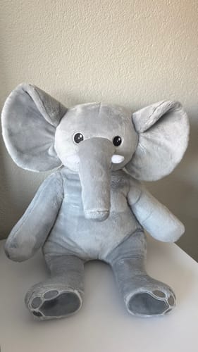 Recensent toont de zachte, grijze Olifant verzwaringsknuffel, die rechtop op een oppervlak zit.