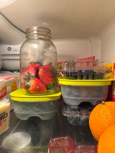 Reviewer's fresh strawberries in a mason jar, sealed with the Mason Genie, next to other containers in a fridge.