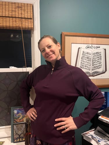 Reviewer smiling while wearing the majestic purple Quinn Ribbed 1/4 Zip, posing indoors to show the comfortable fit.