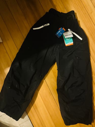 Customer's new black baggy snow pants with tags still attached, laid on a wooden floor.