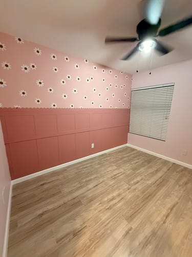 Customer's nursery with pink Camilla Wallpaper featuring a daisy pattern above matching wainscoting.