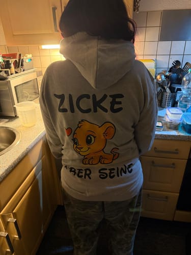 Rückansicht einer Rezensentin, die den grauen Zicke Löwe Hoodie mit dem Aufdruck eines Löwenbabys trägt.