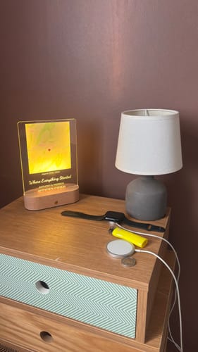 Ein Kunde zeigt die leuchtende, personalisierte 'Notre Moment' Nachtleuchte auf einem Nachttisch.