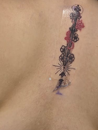 Customer's new vertical tattoo with floral designs, shown after using the brand's pain relief cream.