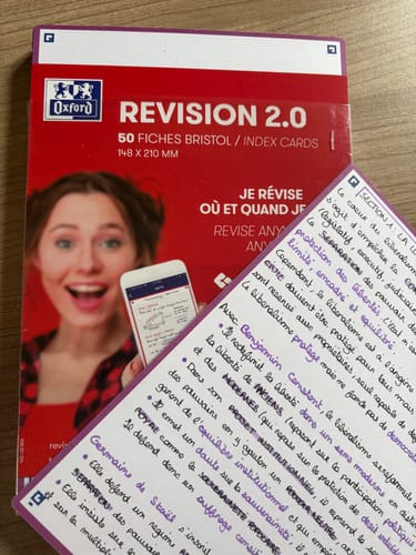 Client montrant une fiche Bristol REVISION 2.0 manuscrite devant l'emballage du produit.