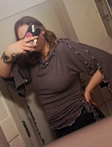 Una clienta se hace una selfie en el espejo con el suéter gris She Shell, mostrando los detalles de los bordes ondulados de color lila.