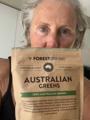 Reviewer holding a paper pouch of Australian Greens Whole Food Powder in front of them, showing the product label.