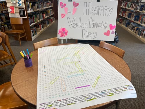 Customer's giant word search puzzle on a round table in a library, partially completed with colorful markers.