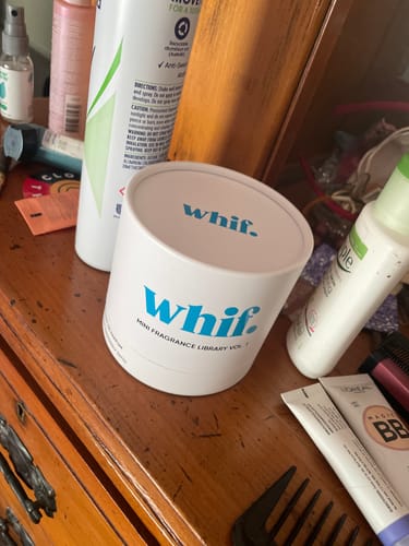 Customer's Fragrance Library Vol. 1 in its white cylindrical box, placed on a wooden vanity among other toiletries.