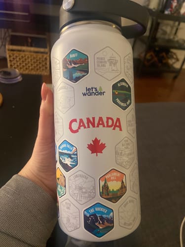 Customer holding the white Canada Bottle, showing several colorful destination stickers applied to the engraved outlines.