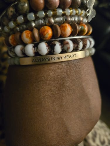 Customer's wrist showing the gold-colored 'Always in my heart' bracelet stacked with other colorful beaded bracelets.