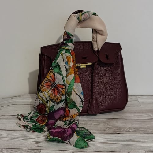 Customer's burgundy pebbled leather Warkin Bag with a colorful patterned scarf tied to the handle, sitting on a wooden surface.