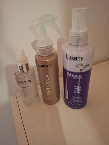 El Serum Antifrizz de Luxeny de un cliente, junto a otros dos productos de la marca sobre una superficie clara.