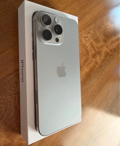 Cliente mostrando su nuevo iPhone 16 Pro Max plateado, parcialmente fuera de su caja sobre una mesa.