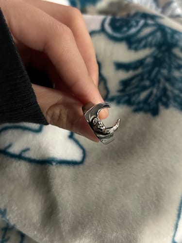 Customer holding a detailed silver-colored ring with a crescent-shaped design between their fingers.