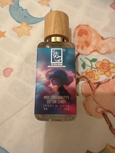 Customer's Miss Congeniality’s Cotton Candy perfume bottle with a wooden cap, shown on a patterned surface.