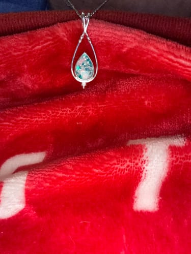 Customer's Double Spade Memorial Pendant with a sparkly blue and white center, resting on a soft red surface.