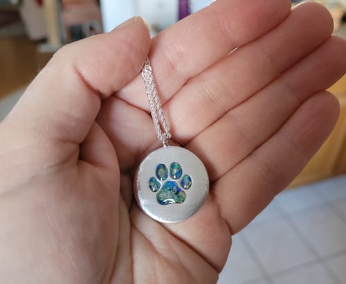 Customer holding the silver Pawprint Disc Pendant in hand, showing the blue and green opal inlay in the pawprint.
