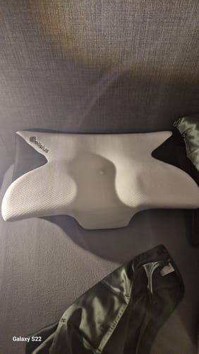 Photo d'un client montrant le coussin d'alignement cervical Cellsius blanc posé sur un canapé.