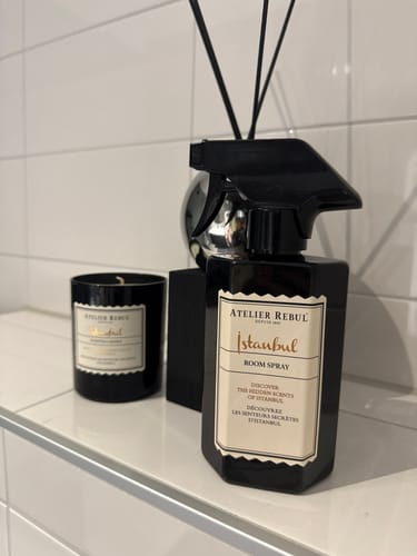 Recensent toont de grote fles Istanbul Roomspray op een witte plank in een badkamer.