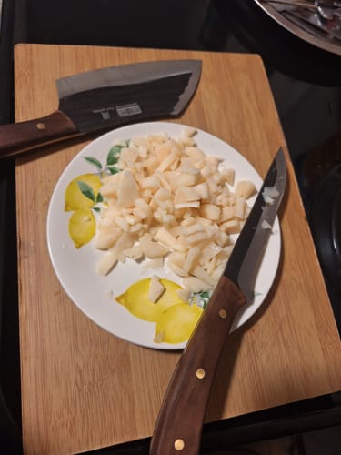 Customer's cleaver and paring knife from the hand forged butcher set on a cutting board with chopped food.