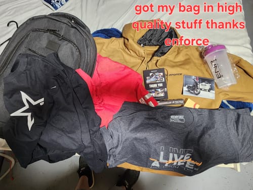 Customer's haul from the Mystery Loaded Backpack, showing various apparel, a shaker bottle, and the backpack on a bed.