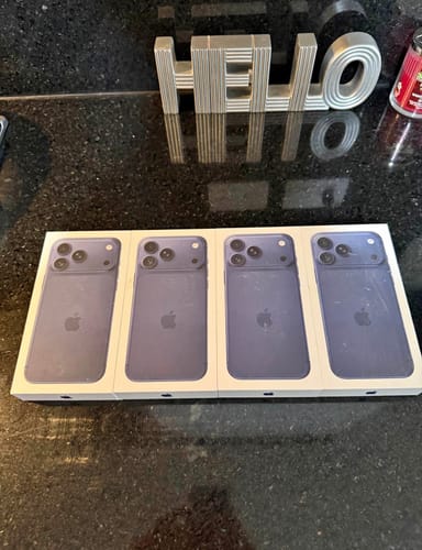 Reseñador muestra cuatro teléfonos IPHONE 17 PRO MAX nuevos y morados en sus cajas sobre un mostrador.