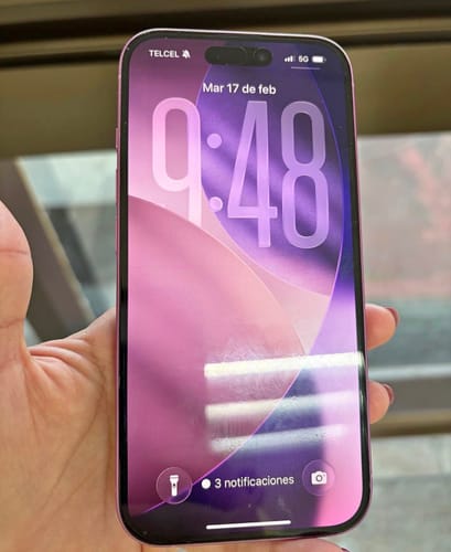 Cliente sosteniendo su iPhone 16 seminuevo de color morado con la pantalla de bloqueo encendida.