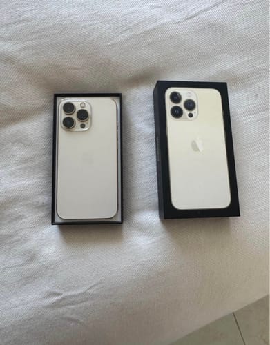 Cliente mostrando dos iPhone 13 Pro plateados en sus cajas abiertas sobre una superficie de tela.