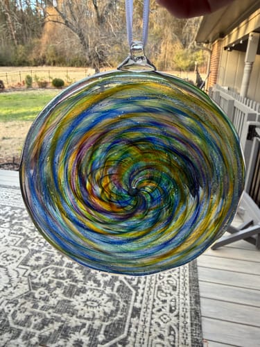 Customer holding a vibrant glass disc suncatcher with a colorful swirl design outdoors.
