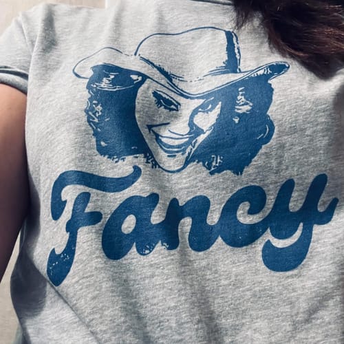 Customer wearing a previously purchased grey t-shirt with a blue graphic of a woman and the word 'Fancy'.