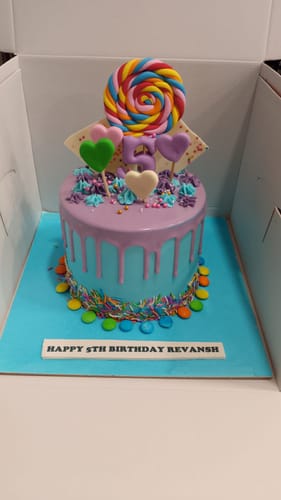 Customer's blue and purple Candy Drip Birthday Cake inside its box, topped with a colorful lollipop and number 5.