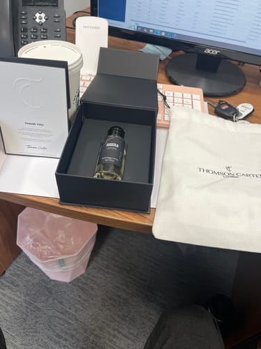 Customer's Smoke & Mirrors Eau de Parfum bottle displayed in its open black box on a desk with its packaging.