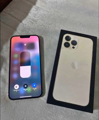Cliente mostrando su iPhone 13 Pro dorado con la pantalla encendida al lado de su caja.