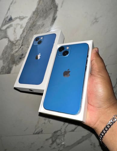 Cliente sosteniendo su nuevo iPhone 13 azul en su caja abierta sobre una superficie de mármol.