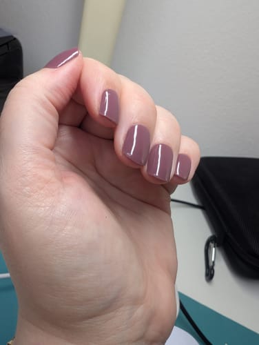 Die Hand einer Kundin mit kurzen, manikürten Nägeln, die die glänzenden UV-Gel-Nagelfolien in Berry Merlot trägt.