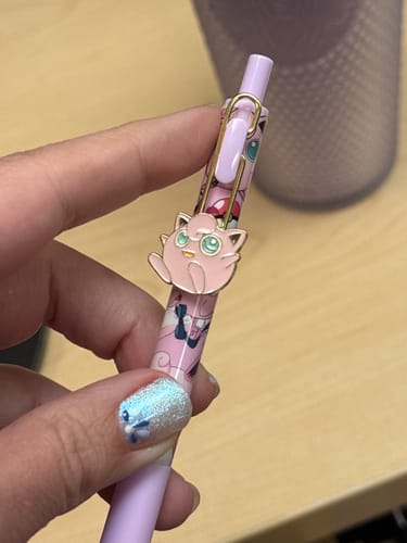 Close-up of a customer holding their pink Pokémon gel pen, showing the cute Jigglypuff pendant on the clip.