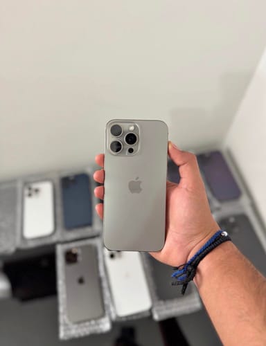 Reseñador sosteniendo un iPhone 16 Pro Max de color gris en su mano, con varios iPhones más en el fondo.