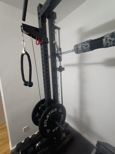 Rezensent zeigt das R7 Plate Loaded Cable System, das mit Gewichtsscheiben beladen an einem Rack montiert ist.